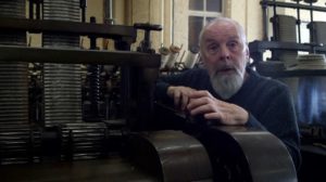 Two screenshots from Paul's film, one of a man's hand on some machinery. In the other the man is facing the camera and leaning on the machine.