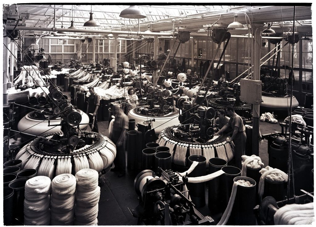 A black and white photograph of works on wool combing machines known as 'Noble Combs' in Salts Mill, Saltaire.