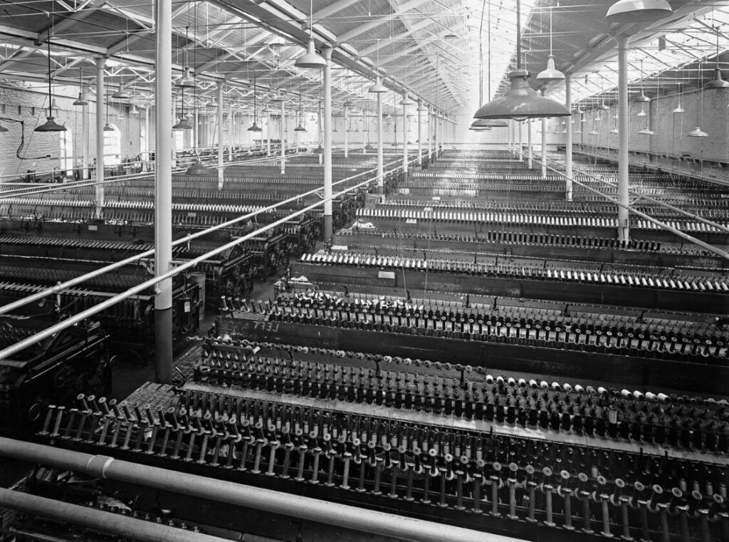 A black and white photo of rows and rows of spinning machinery in a big room at Salts Mill.